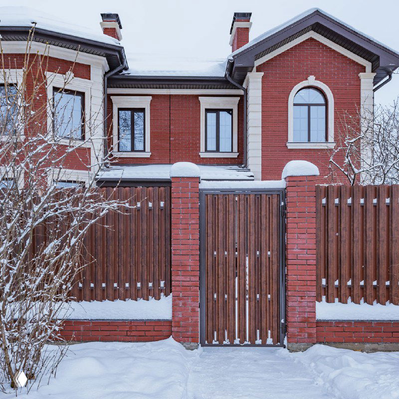 Въезд в частный дом с заснеженной дорогой и воротами — пример проблемной зоны, которую решает система обогрева дорожек REHAU.
