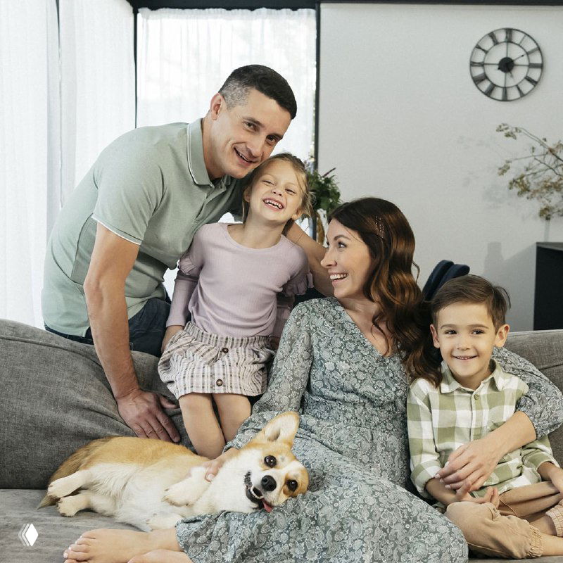 Счастливая семья с детьми и собакой на диване — образ хозяев, которые сократили расходы на отопление и создали комфорт в доме