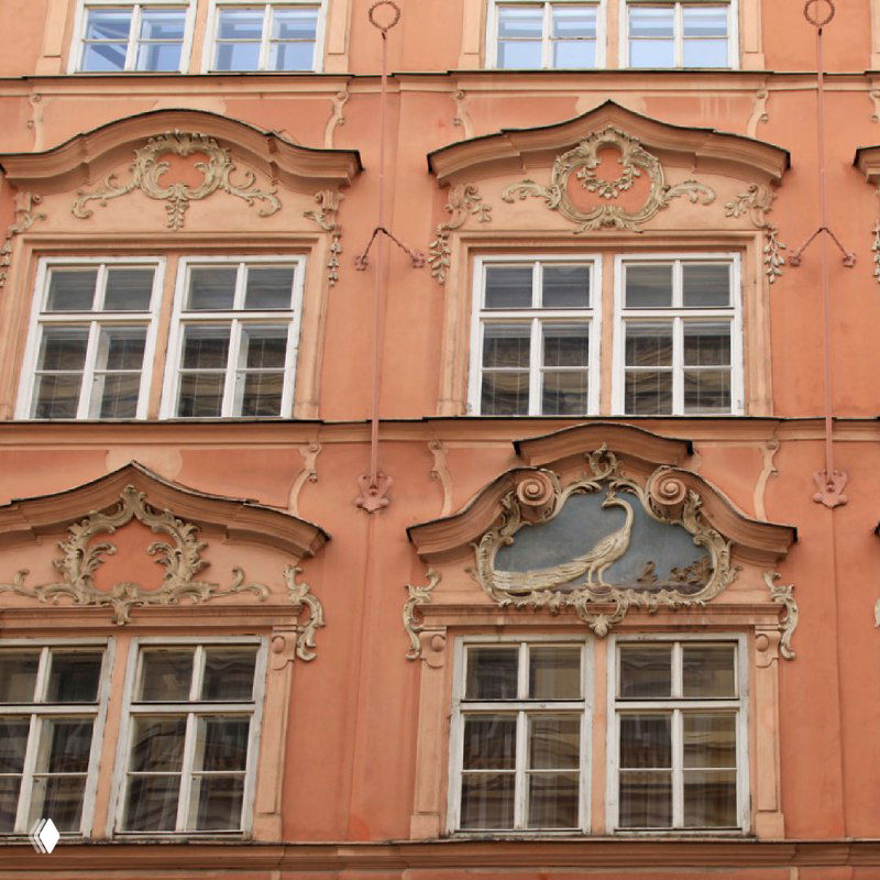 Пастельный фасад с рельефными декоративными наличниками и классическими окнами — близкий план архитектурных деталей и лепнины на стене.