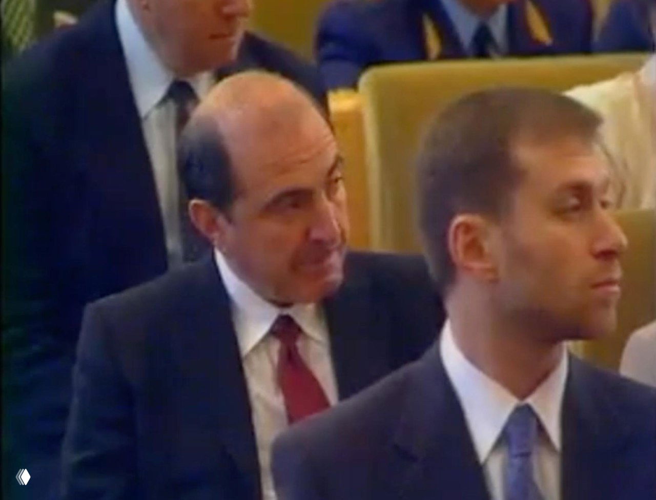 Архивное фото: журналисты и участники в зале заседаний — мужчины в костюмах, серьёзные лица на фоне рядов кресел и слушателей.