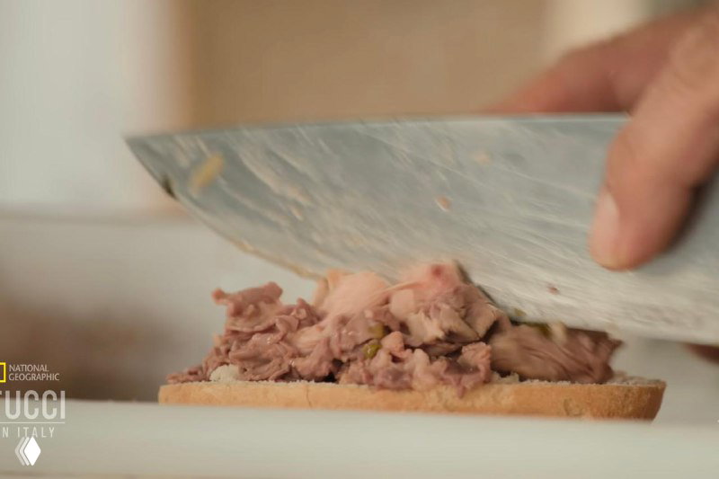 Нож нарезает отварное мясо желудка на кусочки, которые выкладываются на ломтик хлеба в процессе сборки сэндвича