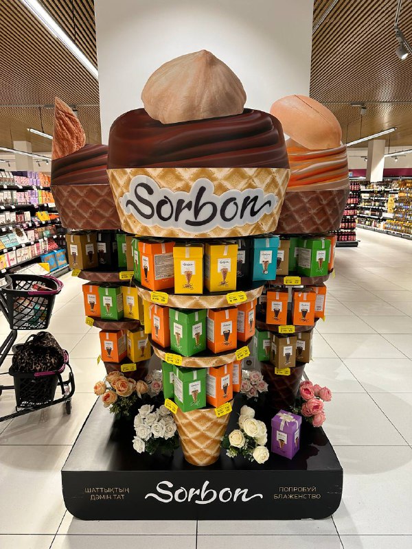 Брендированная стойка с конфетами Sorbon в супермаркете Магнит: большая витрина с яркой упаковкой, полки и проход магазина на заднем плане.