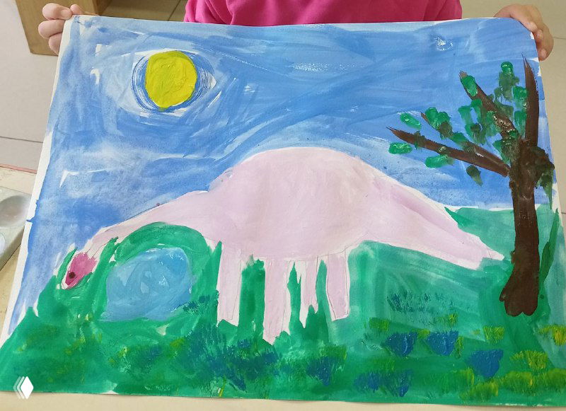 Розовый динозавр на зелёном фоне, выполненный гуашью ребёнком: мягкие мазки, простая композиция и круглая жёлтая деталь в небе, детская работа.