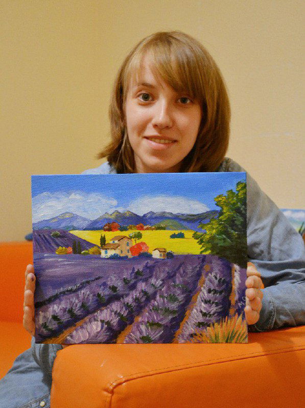 Молодая участница показывает холст с лавандовым полем и горами, законченная студийная работа в пастельных и фиолетовых тонах после занятия
