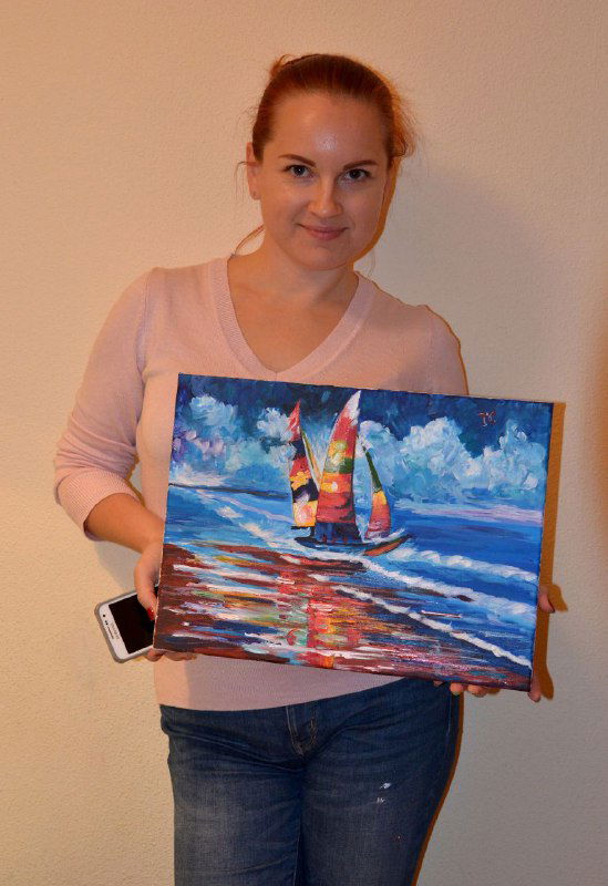Женщина держит холст с морским сюжетом и парусниками, насыщенные синие и красные мазки, пример композиции для взрослых участников мастер-класса