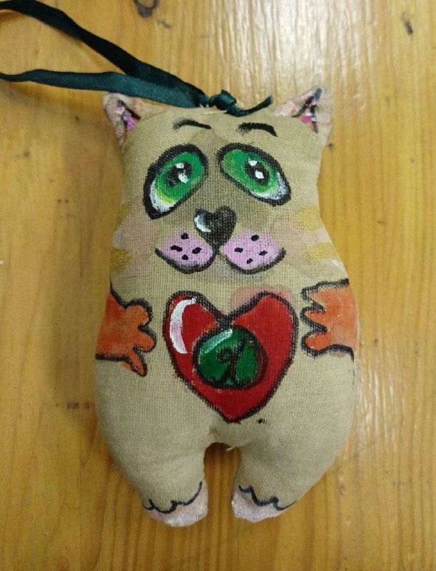 Крупный план расписанной текстильной игрушки-кошки с зелёными глазами; детали лица, мазки акрила и маркерные контуры хорошо видны на бязевой ткани.