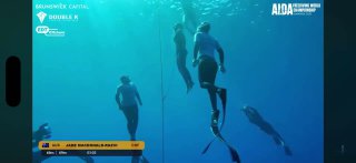 Подводный кадр с соревнований по фридайвингу: несколько спортсменов спускаются вдоль буйка в синей воде, кадр иллюстрирует соревновательную обстановку и судейские решения.