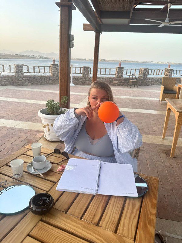 Крупный план женщины-инструктора за столом: она держит оранжевый носодуй и объясняет техники продувки, перед ней блокнот и материалы тренинга по дыханию