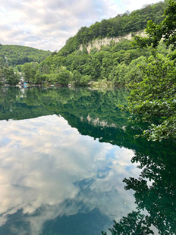 Прозрачное озеро с зеркальной поверхностью, отражающей небо и прибрежные деревья — тихий горный водоём в Кабардино‑Балкарии.