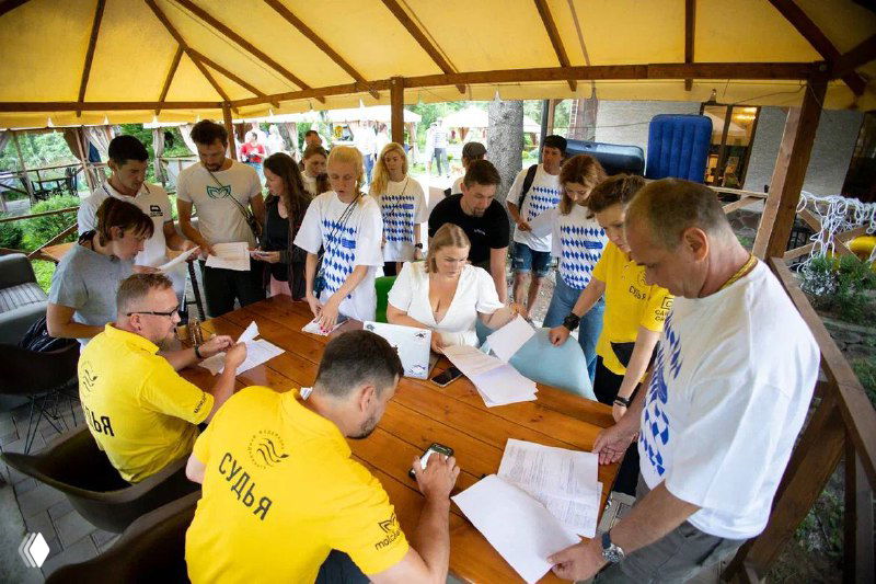 Регистрация спортсменов за длинным столом: судьи и участники заполняют документы, регистрируются и согласуют время стартов перед заплывом.