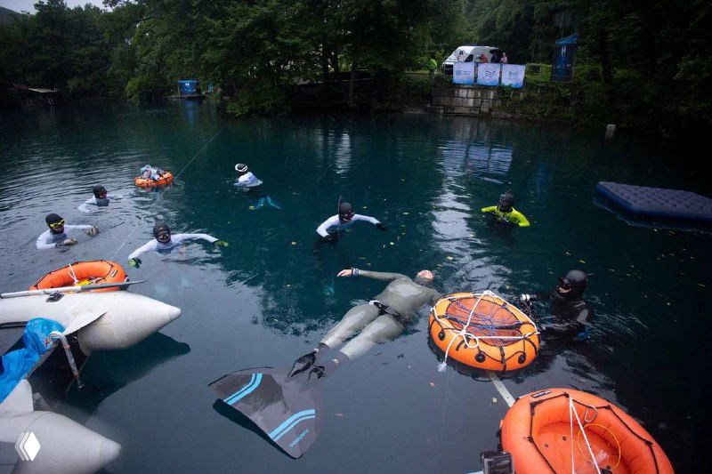 Группа фридайверов и спасательных средств на воде: видны ласты, буи и надувные круги вокруг зон старта и контроля безопасности.