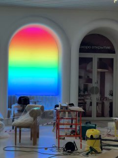 Интерьерный фрагмент с аркой и радужной подсветкой, строительные леса и техника на фоне процесса отделки помещения