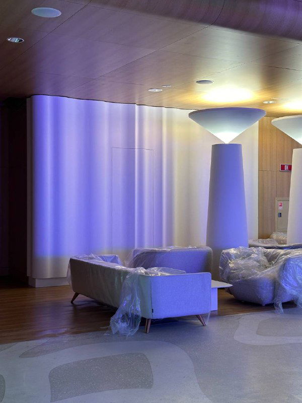 Зал с мягкой подсветкой и мебелью в плёнке, кадр показывает стадию подготовки интерьера и завершающие работы перед уборкой