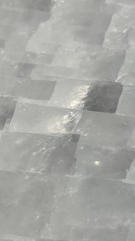 Крупный план мозаичной поверхности оникса: полупрозрачные белые и серые пластины, заметен характерный блеск и пересекающиеся швы камня.