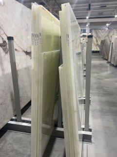 Листы оникса на складе: вертикальные пластины камня на стойках, представлены разные оттенки и текстуры до обработки и установки.