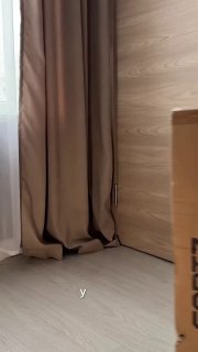 Превью видео‑отзыва: угол комнаты с бежевой шторай, светлым ламинированным полом и картонной коробкой — намёк на распаковку пылесоса.