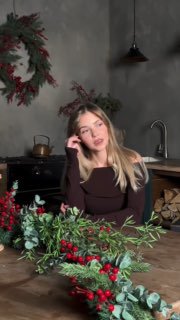 Девушка за столом с праздничным венком и декором в кухонной студии — кадр, создающий атмосферу уютного домашнего обзора техники.