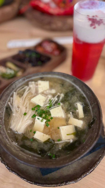 Глубокая миска мисо-супа с тофу, эноки и зелёным луком, чаша на деревянном столе в интерьере японского ресторана.