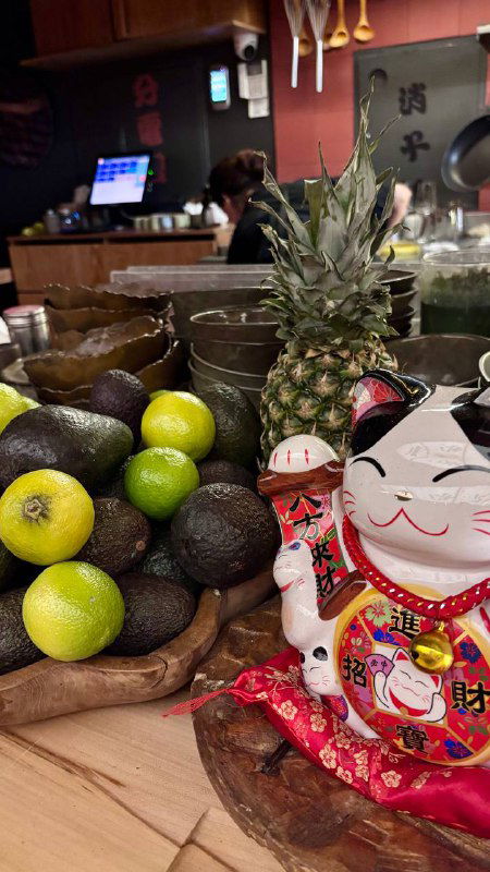 Декоративная композиция на стойке: ананас, авокадо, лаймы и фигурка манэки-нэко — детализация оформления ресторана в японском стиле.