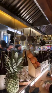 Открытая кухня и полки с бутылками саке, повара и подсобная зона видны за стойкой — атмосфера живой гастрономии.