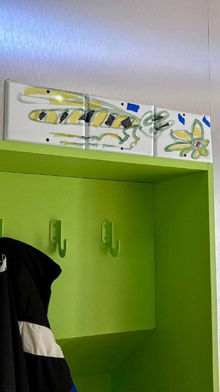 Зелёная гардеробная ниша с крючками и декоративными керамическими панно над ней в интерьере кофейни 2046, акцент на деталях оформления.