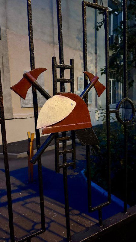 Граффити или арт-объект с изображением топоров и декоративных элементов на металлической ограде — уличное творчество района поблизости.