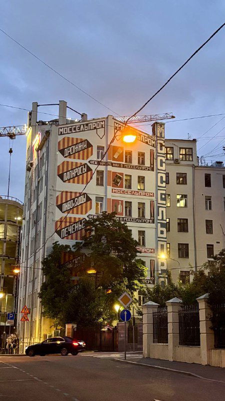 Большая настенная роспись и архитектурные фасады на фоне вечернего неба — городской пейзаж в районе Большого Кисловского переулка.