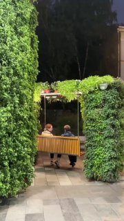 Деревянная скамейка-качели, обвитая зеленью и растениями, на тихой аллее — финал прогулки после ужина в Layerz.