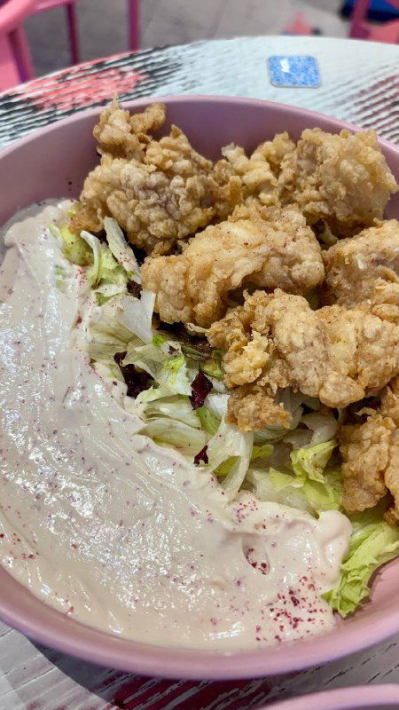 Тарелка с панированной треской — кусочки золотистой рыбы на салатной подложке и соус, подача в пастельной посуде на розовом фоне.