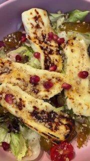 Деталь салата с жареным халуми: полоски сыра с поджаренной корочкой, гранатовые зёрна, томаты черри и хрустящие листья салата.