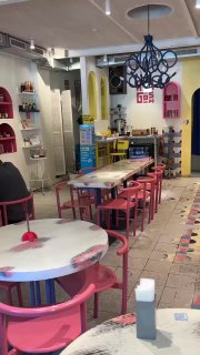 Интерьер кафе Абу Гош: розовые и пастельные столы, стулья и декоративные элементы, светильник и открытое пространство для гостей.