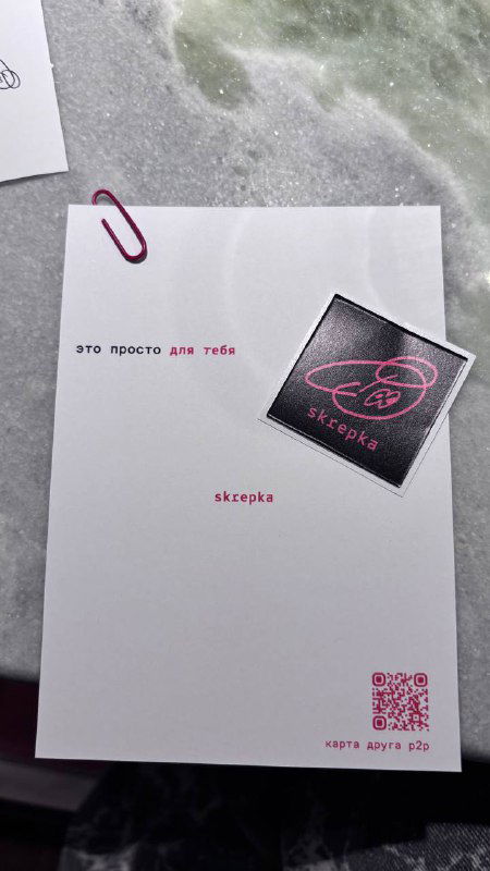 Открыточка и фирменная наклейка Skrepka на белой бумаге: мелкие детали брендинга, бумажная скрепка и аккуратная типографика на столе.