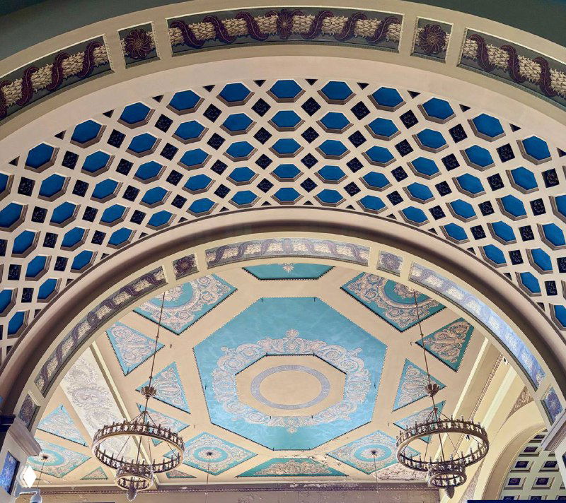 Роспись и украшенный овальный купол большого зала вокзала с люстрами и геометрическим орнаментом, вид снизу на декоративную подсветку и роспись.