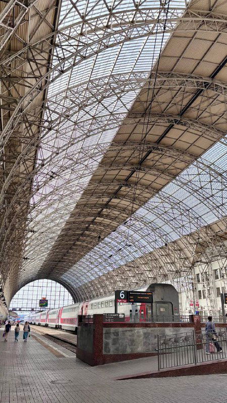 Арочная стальная кровля дебаркадера над путями Киевского вокзала: длинная перспектива платформы, вагон на путях и железная конструкция крыши.