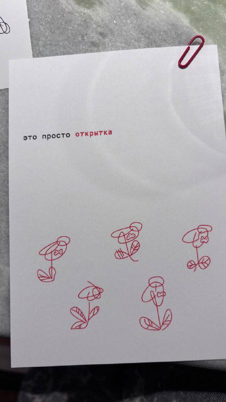 Лист бумаги с простыми красочными скетчами цветов и надписью, зажатый красной скрепкой на мраморном столе, элемент фирменного стиля.