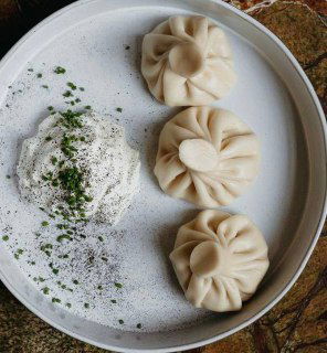 Тарелка с аккуратно сложенными хинкали и порцией кремового соуса — классическая подача пельменей по-грузински в Bagebi.
