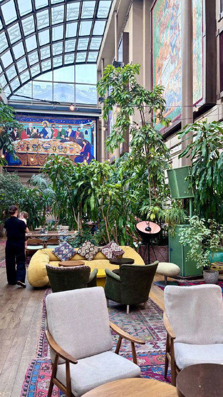 Верхнее пространство ресторана под стеклянной крышей с обилием зелени, мягкой мебелью и художественными элементами — пекарня и лаунж Bagebi.