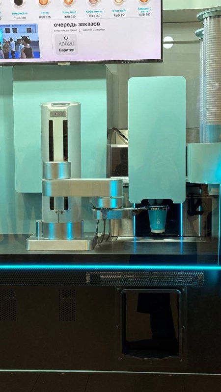 Деталь механизма с держателем стаканчиков и соплом для налива кофе внутри автомата «Робот-бариста», видна зона подачи напитка на подставку.