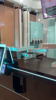 Стеллаж с одноразовыми стаканчиками и зона выдачи напитка в автомате, подсветка и прозрачные панели видны на снимке.