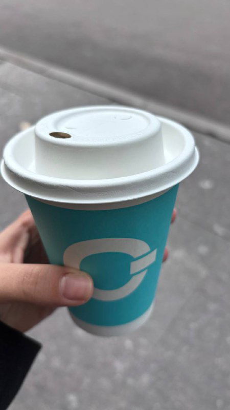 Рука держит одноразовый стакан с крышкой и бирюзовым бумажным стаканом с логотипом — фото готового напитка после покупки у автомата «Робот-бариста».