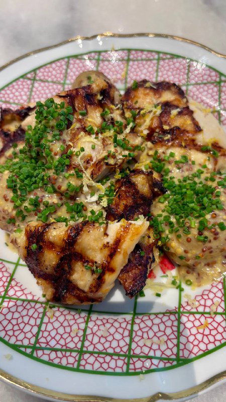 Блюдо с запечёнными или обжаренными кусочками рыбы или мяса с кремовым соусом и рубленой зеленью в декоративной тарелке.