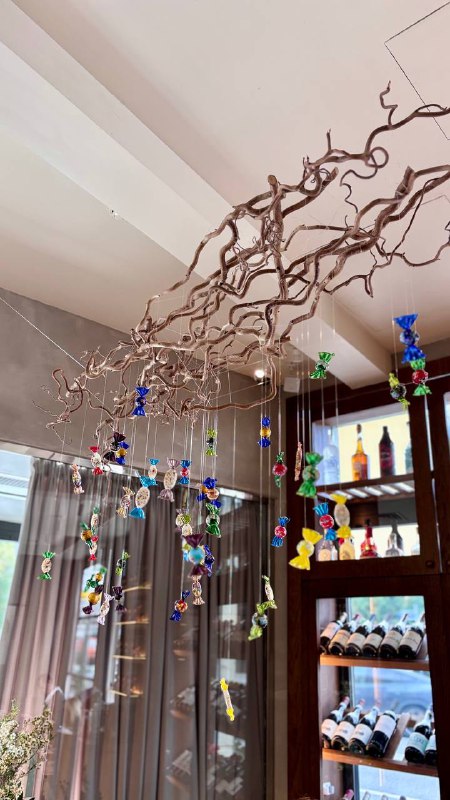 Декоративные подвесные украшения и полки с бутылками в интерьере ресторана — художественная инсталляция у окна.