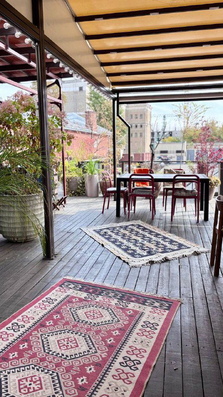 Открытая веранда ресторана Kilim в Красном Октябре: коврики, столы и деревянная пергола, вид на набережную и городской пейзаж в Москве.