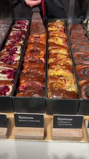 Крупный план бриошей в витрине: корочка, яркие начинки и текстура булочек, видно оформление и часть табличек с названиями.