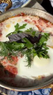 Блюдо с яйцом в томатном соусе, запечённое в небольшой сковороде и украшенное зеленью и базиликом, подано на столе Kilim в Москве.