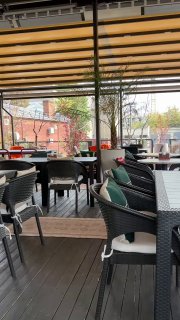 Веранда Kilim: столы и стулья под деревянной перголой, городская улица и краснокирпичные здания на заднем плане, ощущение летнего завтрака в Москве.