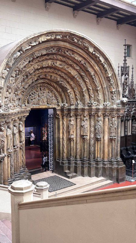 Арочный портал из резного камня внутри экспозиции: детальная резьба и фигурные налепы, виден проход в следующую залу музея.