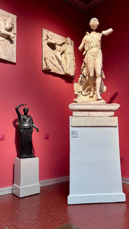 Красный зал Пушкинского музея с несколькими статуями и бархатистой стеной: контраст тёплого света и белых форм скульптур.