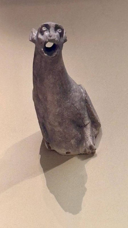 Маленькая скульптура-горгулья or карикатурная фигура на стене экспозиции, тёмный силуэт отбрасывает выразительную тень на фоне светлой стены.