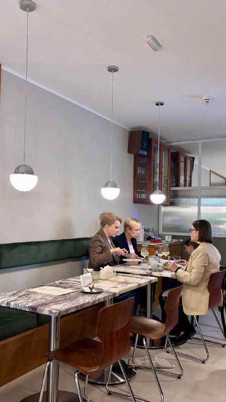 Гости за столом в зале Сentrale Bistro: люди дегустируют блюда в светлом современном интерьере с мраморными столами и подвесными светильниками.